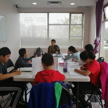 Students seated together around a large table in a classroom with big windows